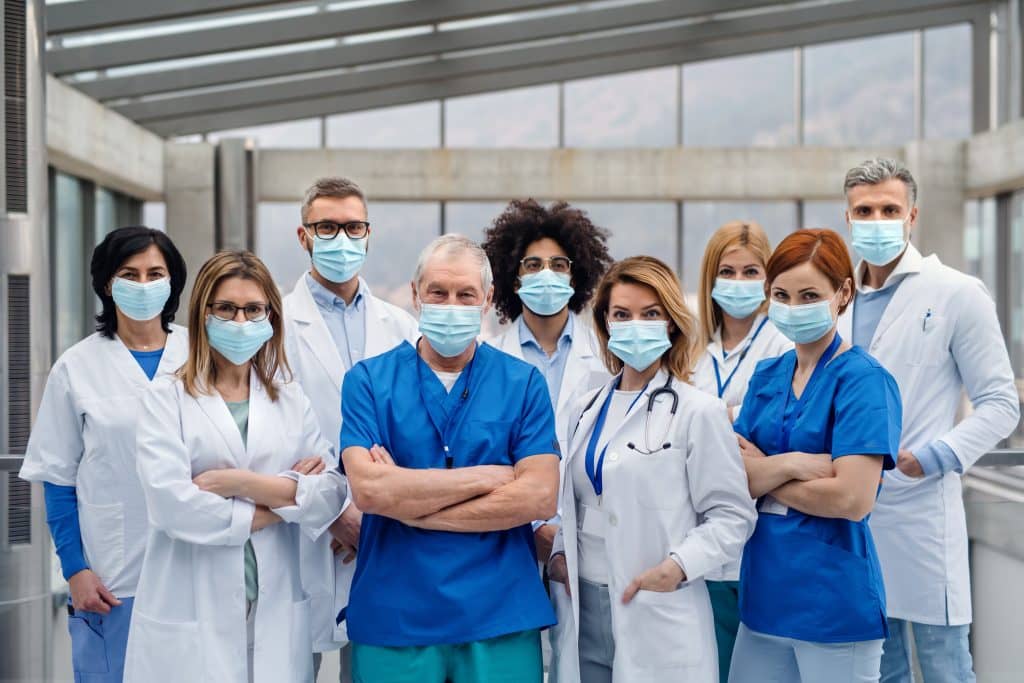 People wearing blue scrubs and white lab coats with surgical face masks on, in a group photo
