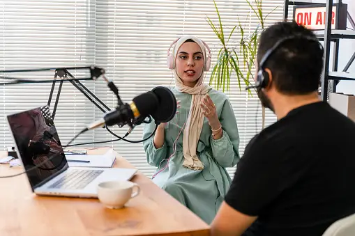 A lady wearing a hijab being interviewed by a male in a podcast recording setting